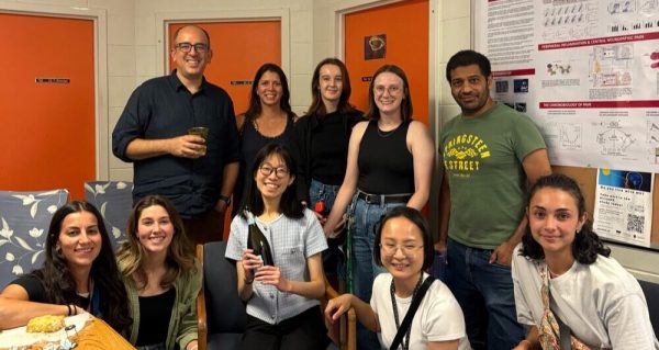The lab members sitting/standing around Ruilin, who is sitting in the middle holding a bottle of champagne